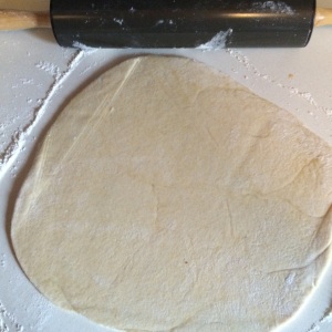 Roll back and forth with your rolling pin for a few strokes, then give the dough a quarter turn and roll again for an even stretch. Keep going until you have a rough circle.